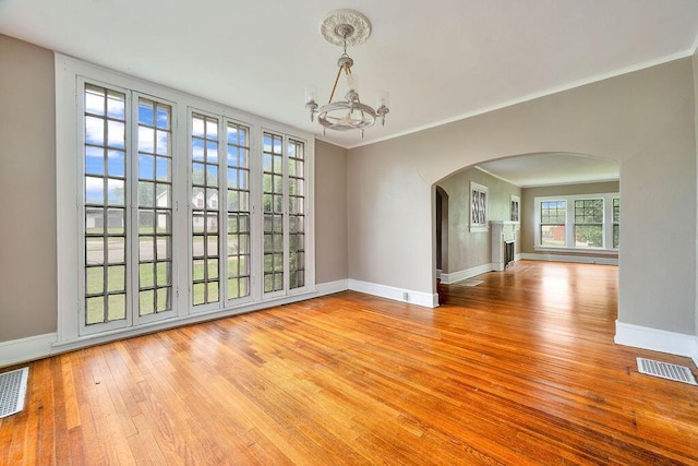 unfurnished dining area featuring arched walkways, a chandelier, hardwood / wood-style floors, baseboards, and crown molding