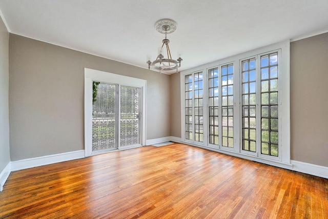 unfurnished room with a chandelier, baseboards, wood finished floors, and crown molding