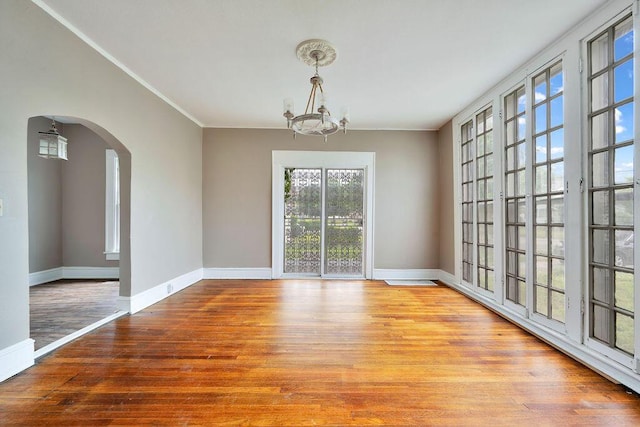 unfurnished dining area with wood finished floors, a chandelier, arched walkways, baseboards, and crown molding