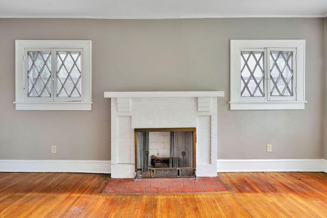 unfurnished living room with hardwood / wood-style floors, baseboards, ornamental molding, and a brick fireplace