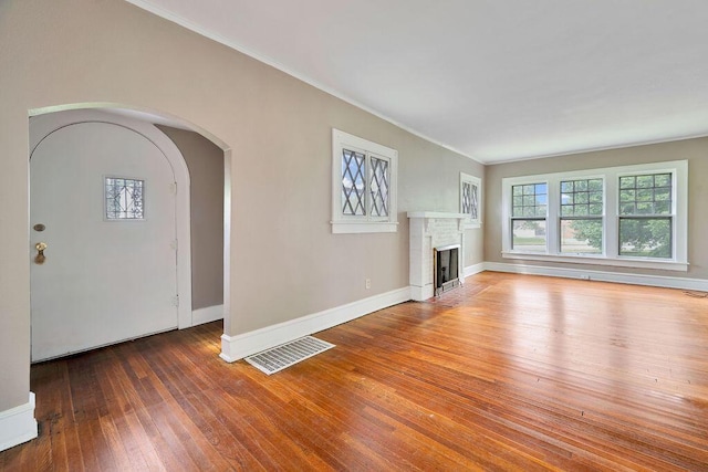 unfurnished living room with crown molding, a brick fireplace, hardwood / wood-style flooring, arched walkways, and baseboards