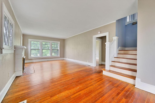 unfurnished living room featuring hardwood / wood-style floors, stairway, crown molding, baseboards, and a fireplace