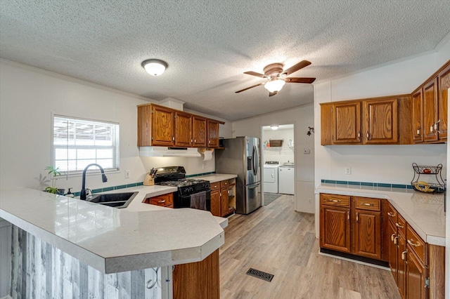 kitchen with independent washer and dryer, stainless steel fridge, a sink, black range with gas cooktop, and under cabinet range hood