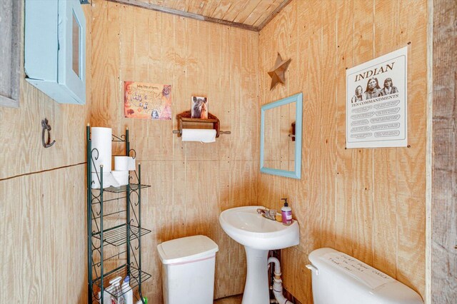half bath featuring wooden walls, toilet, and a sink