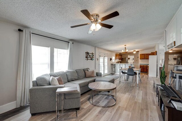 living room featuring light wood-style flooring, a textured ceiling, and ceiling fan with notable chandelier
