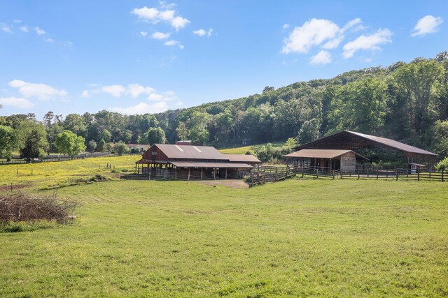 view of yard featuring an exterior structure, a pole building, a rural view, a view of trees, and an outbuilding