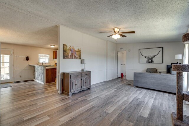 living area with a ceiling fan, a textured ceiling, wood finished floors, and a decorative wall