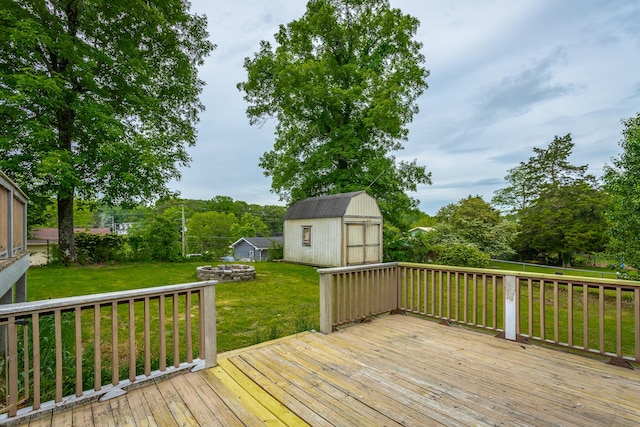 deck featuring fence, an outbuilding, a shed, a lawn, and an outdoor fire pit