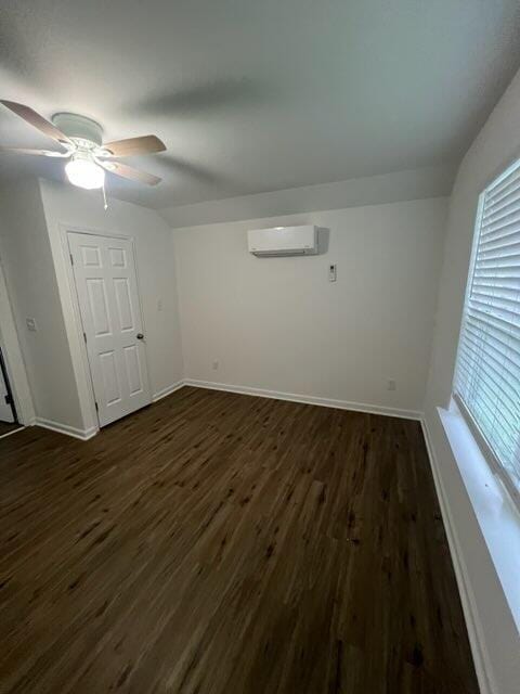 empty room with baseboards, ceiling fan, an AC wall unit, and dark wood-type flooring