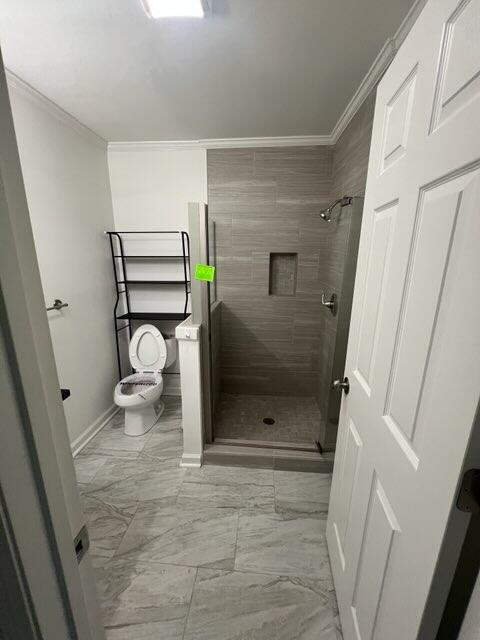 bathroom featuring crown molding, marble finish floor, toilet, baseboards, and a shower stall