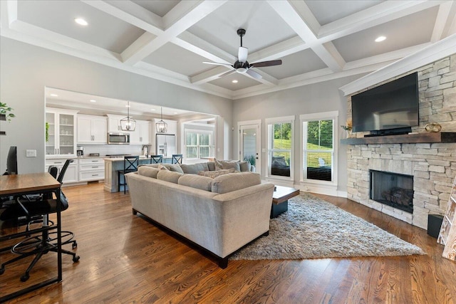 living area with beamed ceiling, a stone fireplace, dark wood-type flooring, recessed lighting, and a ceiling fan