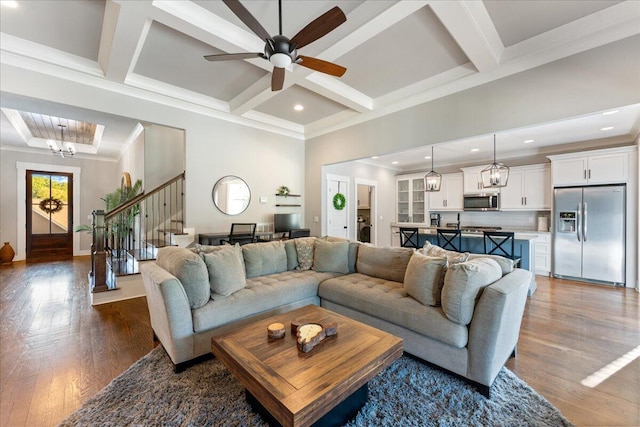 living room with a ceiling fan, dark wood-type flooring, ornamental molding, stairway, and coffered ceiling