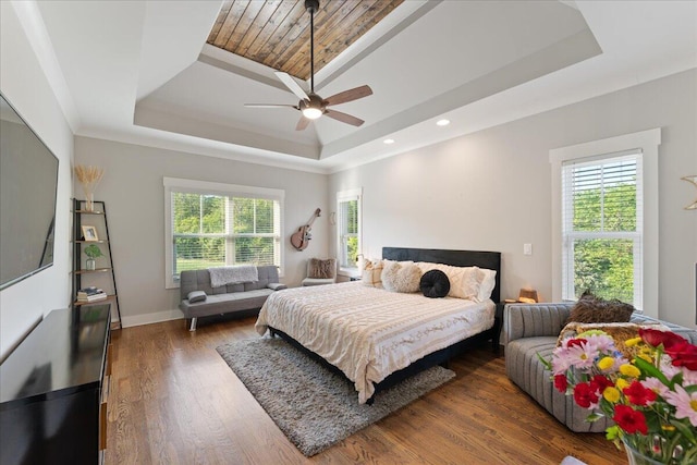 bedroom with multiple windows, a ceiling fan, a tray ceiling, and wood finished floors