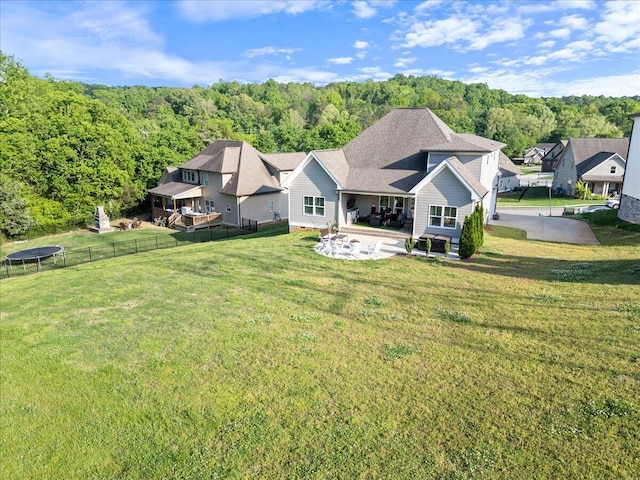 back of property featuring a patio, a view of trees, a lawn, and fence