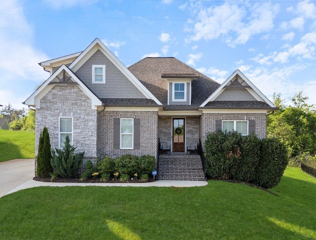 craftsman inspired home featuring brick siding, stone siding, a front yard, and roof with shingles