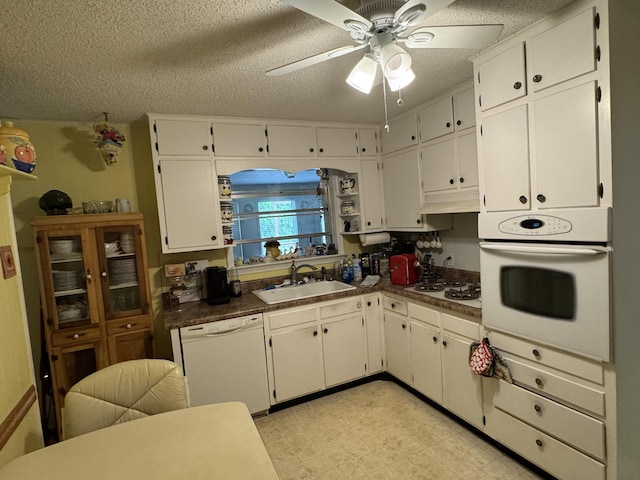 kitchen with white appliances, a ceiling fan, dark countertops, and a sink