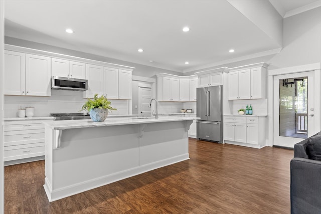 kitchen featuring white cabinets, a sink, an island with sink, stainless steel appliances, and backsplash