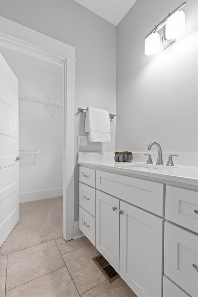 bathroom with a walk in closet, vanity, tile patterned floors, baseboards, and visible vents