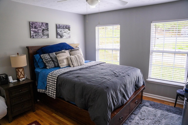 bedroom featuring baseboards, a ceiling fan, wood finished floors, and multiple windows