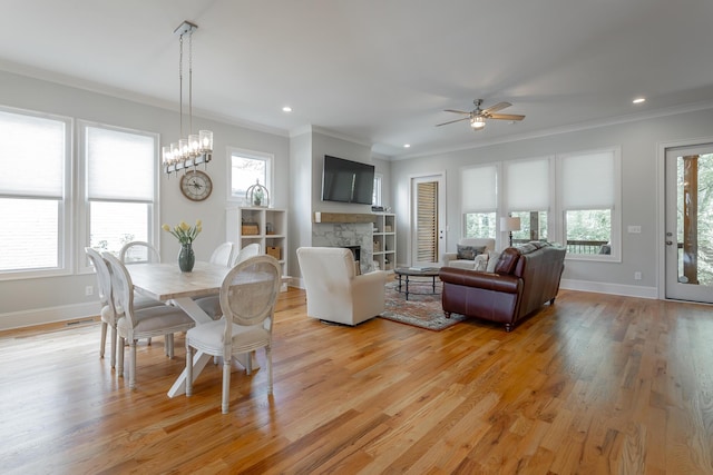 dining space featuring crown molding, ceiling fan, a stone fireplace, and baseboards
