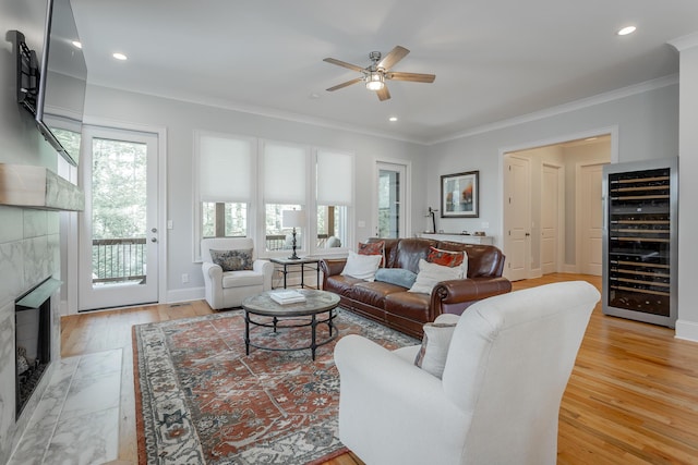 living room featuring wine cooler, crown molding, ceiling fan, and a premium fireplace