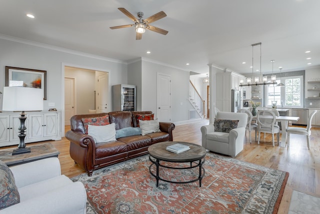 living area featuring stairway, ornamental molding, light wood-style floors, and a ceiling fan