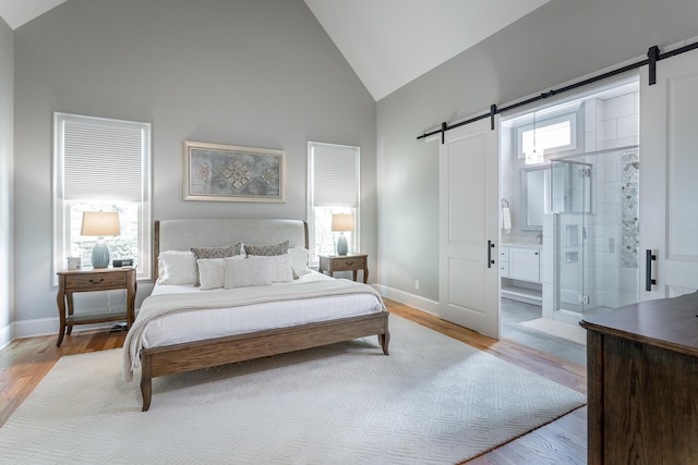 bedroom with high vaulted ceiling, baseboards, light wood finished floors, and a barn door