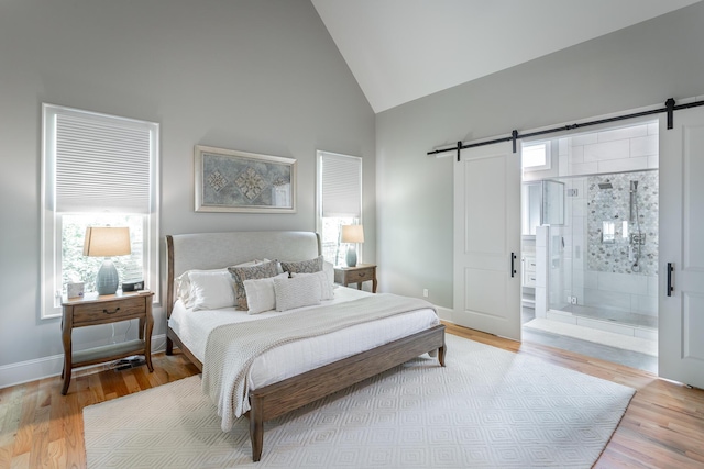 bedroom featuring wood finished floors, baseboards, high vaulted ceiling, a barn door, and ensuite bath