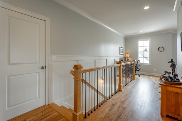 hallway with a wainscoted wall, recessed lighting, an upstairs landing, wood finished floors, and ornamental molding
