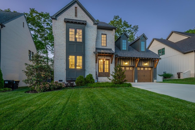 view of front facade featuring a lawn, brick siding, driveway, and french doors