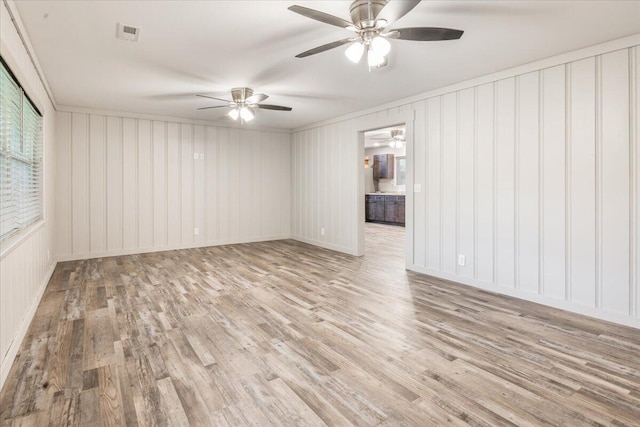 empty room featuring crown molding, a ceiling fan, wood finished floors, and visible vents