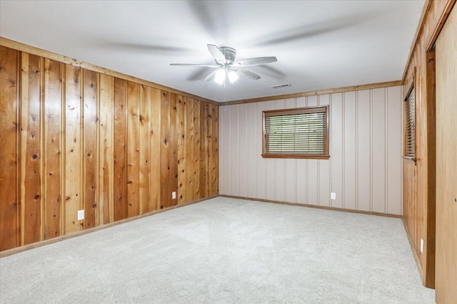 spare room featuring visible vents, carpet flooring, ceiling fan, and wood walls