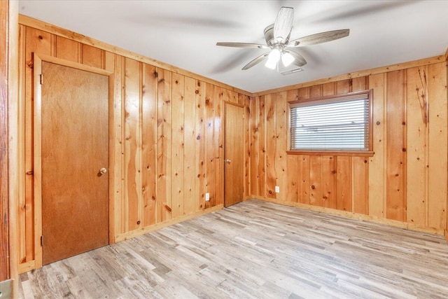 unfurnished room featuring wooden walls, ceiling fan, and light wood finished floors