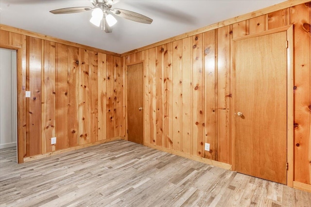 empty room with wooden walls, a ceiling fan, and wood finished floors