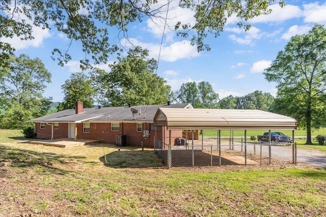 rear view of house with a lawn, a detached carport, central AC, and driveway
