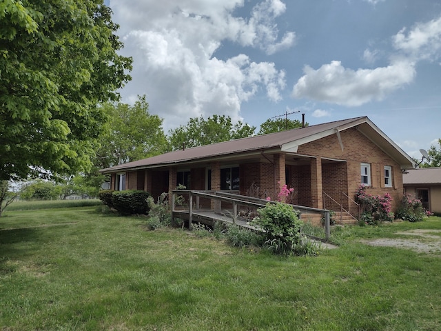 rear view of house with covered porch, a yard, and brick siding