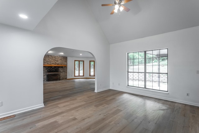 unfurnished living room with visible vents, a ceiling fan, wood finished floors, high vaulted ceiling, and arched walkways