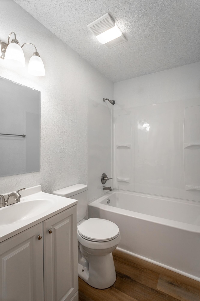 full bath with vanity, shower / bathtub combination, toilet, a textured ceiling, and wood finished floors