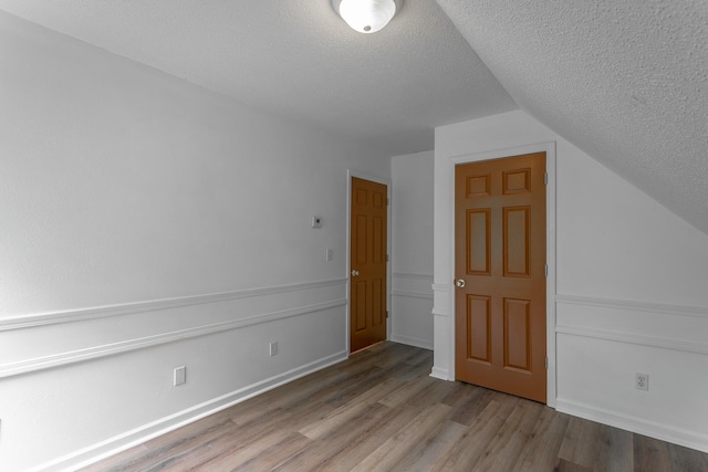 additional living space featuring baseboards, a textured ceiling, wood finished floors, and lofted ceiling