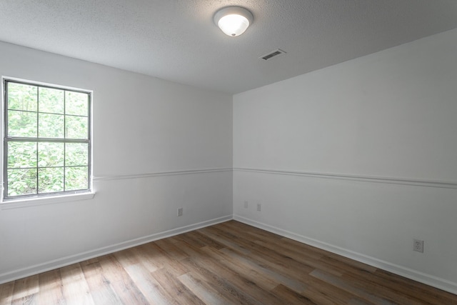 empty room featuring baseboards, a textured ceiling, wood finished floors, and visible vents