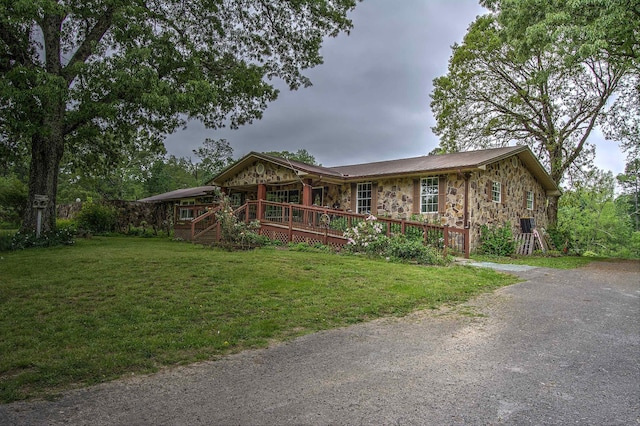 ranch-style home featuring stone siding, a deck, a front yard, driveway, and metal roof