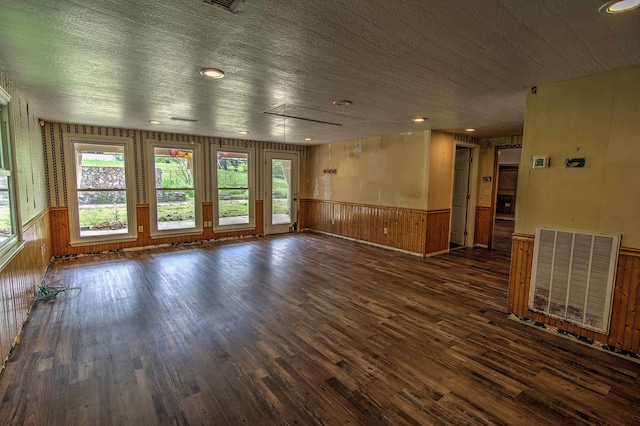 empty room with wooden walls, a wainscoted wall, wood finished floors, and visible vents