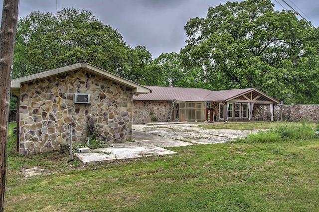 back of property with a lawn, a patio, metal roof, and stone siding