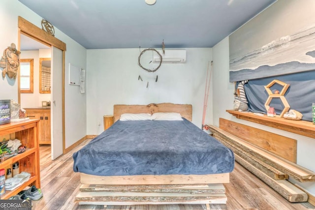 bedroom with ensuite bathroom, wood finished floors, and an AC wall unit