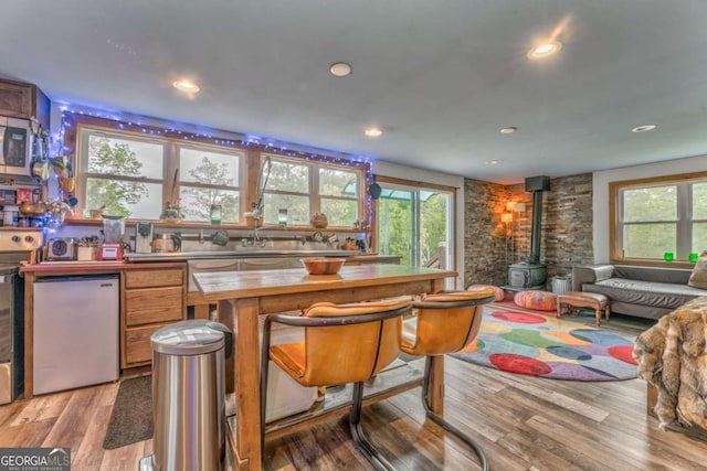 bar with light wood finished floors, a wood stove, recessed lighting, stainless steel microwave, and bar area