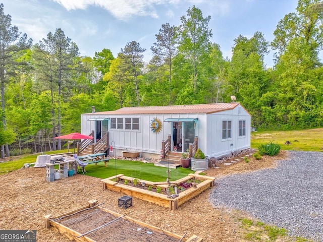 back of property featuring board and batten siding, a forest view, a garden, and entry steps
