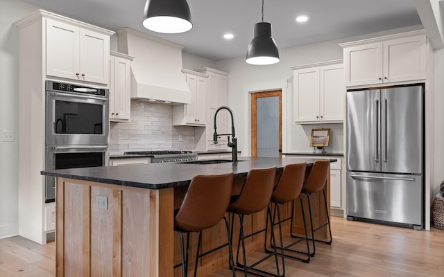 6949 Sawyer Rd, Signal Mountain, TN 37377 - kitchen featuring stainless steel appliances, dark countertops, decorative backsplash, light wood-style flooring, and a kitchen island with sink