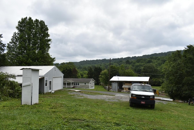 view of grassy yard featuring a garage, a view of trees, and driveway