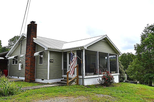 view of front facade featuring a chimney, crawl space, a sunroom, metal roof, and a front lawn