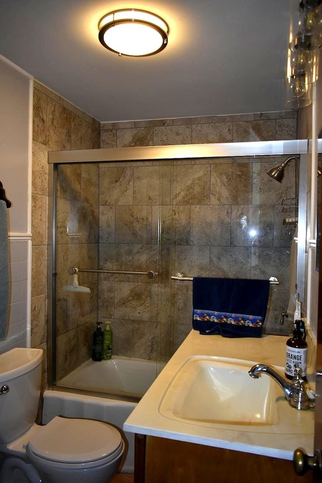 full bath featuring toilet, vanity, combined bath / shower with glass door, and tile walls